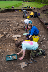 Researchers and students working at an archaeological dig site, on hands and knees digging into earth and assessing archaeological finds