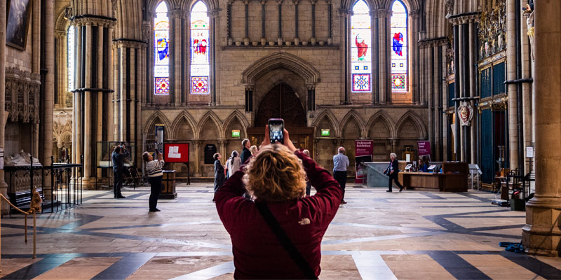 Woman taking a photo of a stained glass window inside a church. 