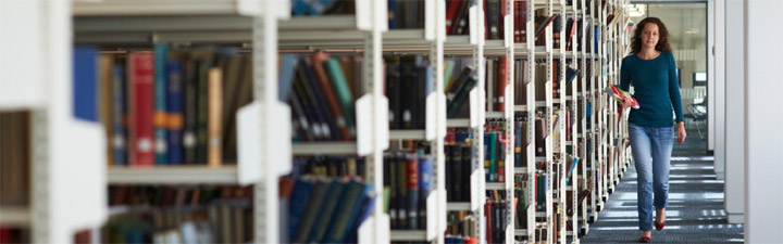 A student walking past shelves in the library. Photo by John Houlihan