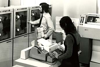 Photo of computing equipment and two members of Computing Service staff at the University in the early 1970s.