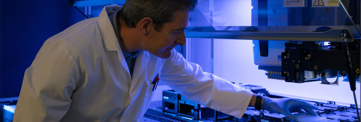 a man reaches into a marge microscope enclosure to retrieve a petri dish