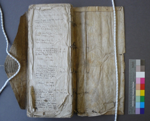 Limp parchment covered parish register, open to display damaged paper pages, with a colour calibration card alongside (PR/BP/6)