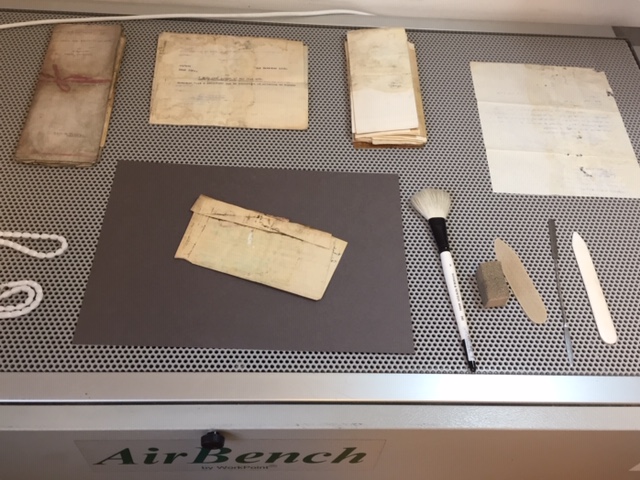 Mouldy documents on a perforated air bench, along with a brush, smoke sponge and various spatulas.