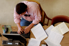 Image of man in pink shirt studying with notebooks and computer