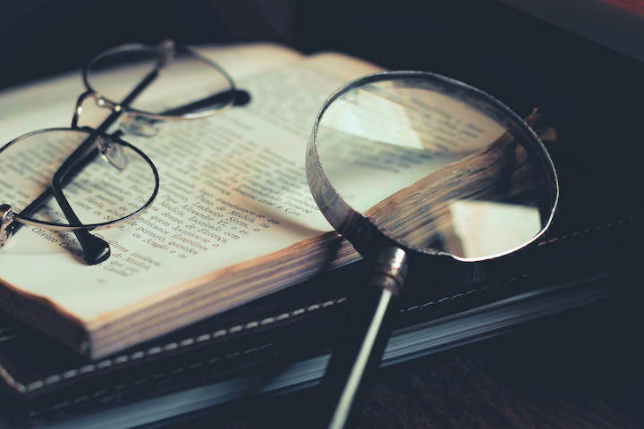 An open book with a magnifying glass and a pair of glasses