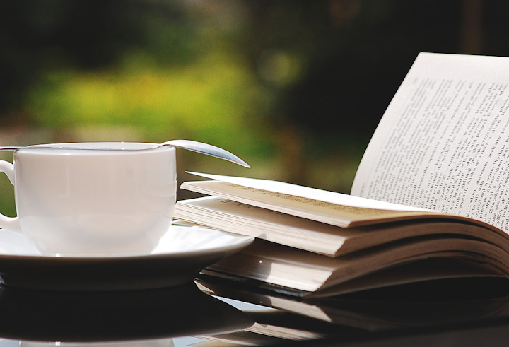 A cup of tea and an open book on a table in a garden