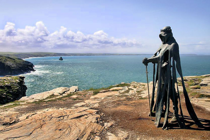Bronze sculpture on Tintagel cliffs of a tall, cloaked and crowned figure leaning on a sword, titled 'Gallos', by Rubin Eynon.