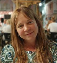 Dr Stephanie Mawson smiling gently, and a long-haired person in a patterned top in a busy indoor space.