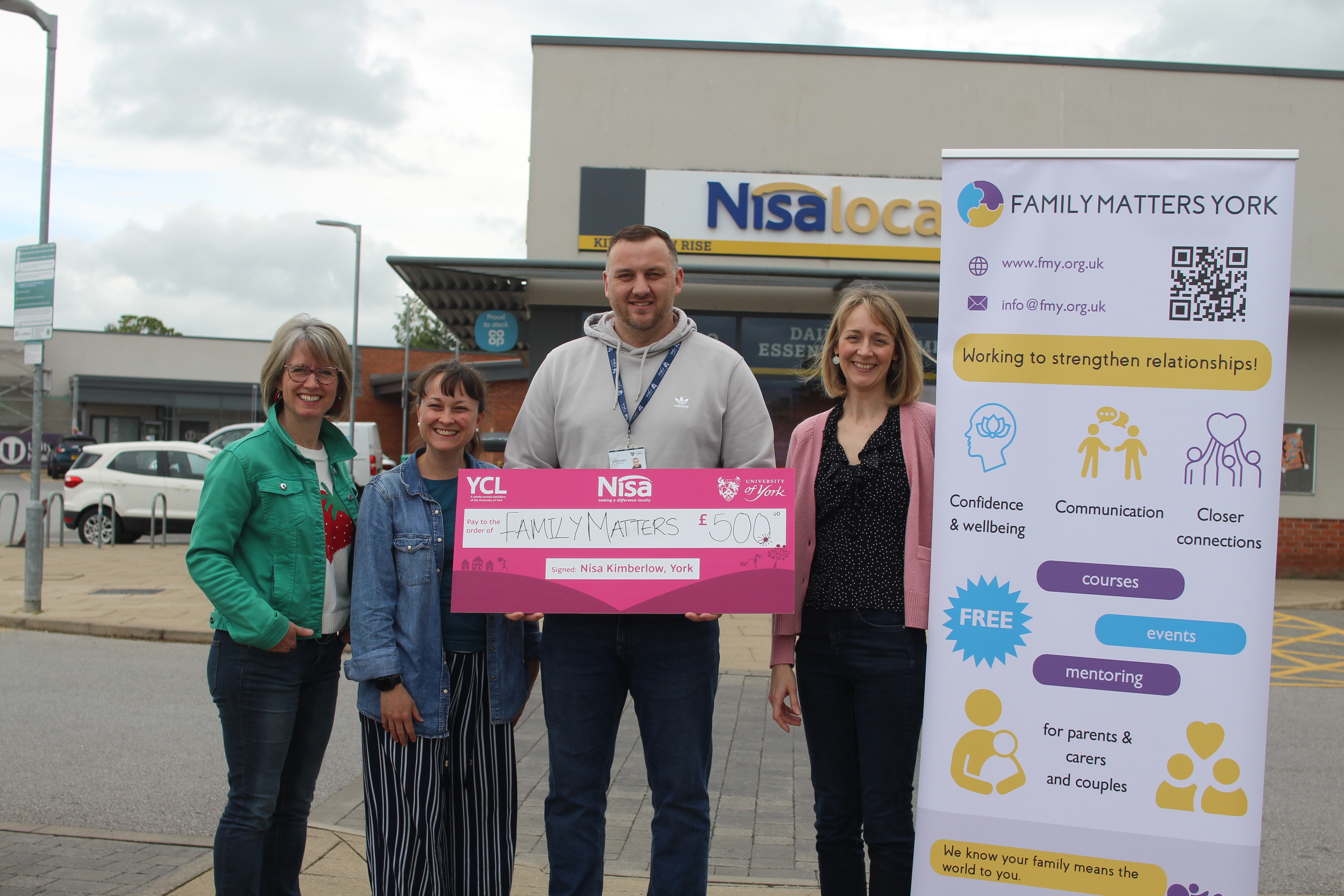 Four people standing outside a Nisa Local store, holding a large ceremonial donation cheque for £500 made out to 