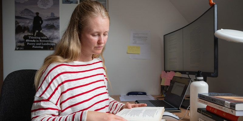 A postgraduate researcher reading a book at her desk.