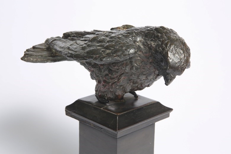 Bronze sculpture of a hawk, on the ground, looking down