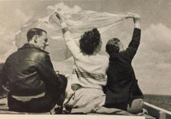 Image of a man and two women on a boat with their backs to the camera, the women holding a white cloth which is blowing in the wind.Photo credit  © The Rowntree Society