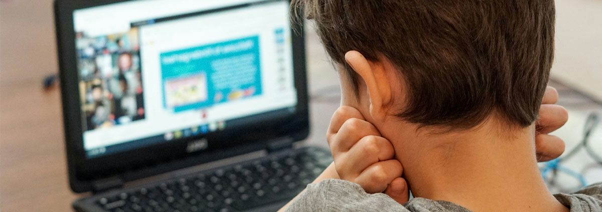 A young boy looks at his laptop screen with his head in his hands