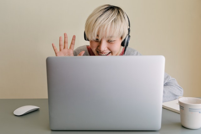 A woman waves at a laptop