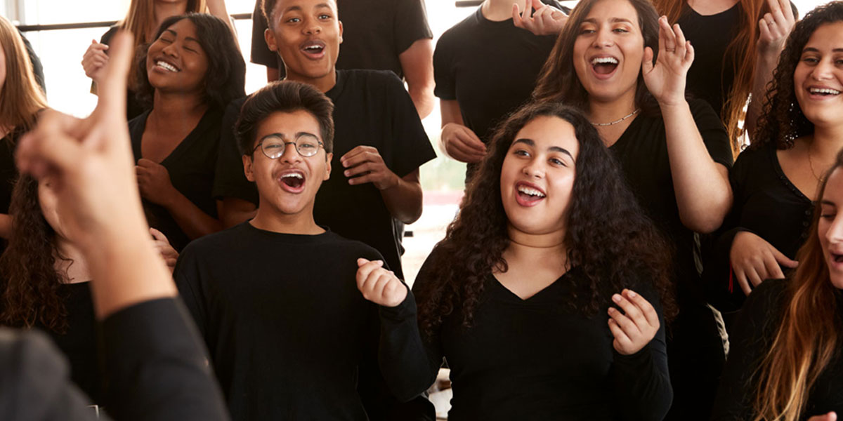 A choir, lead by the choirmaster in the foreground, at rehearsal.