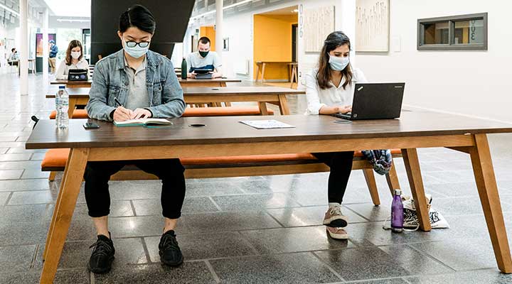 Students working in a group wearing face coverings and keeping 2 metres apart