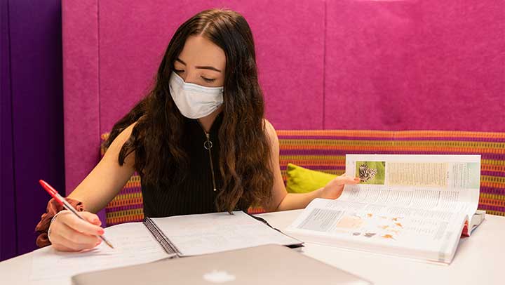 A student wearing a face covering while she studies inside