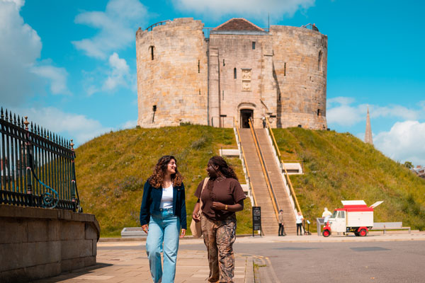 Two students walking past Clifford's Tower in York