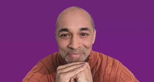 Robin Sundaram, resting his chin on his clasped hands, against a purple background