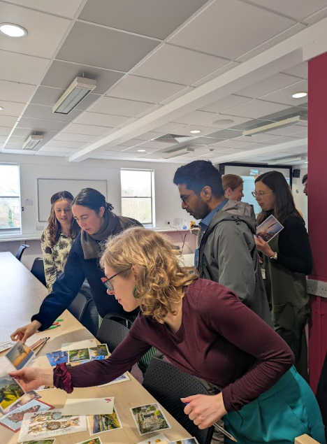 A group of attendees interacting with a table full of postcards and photos