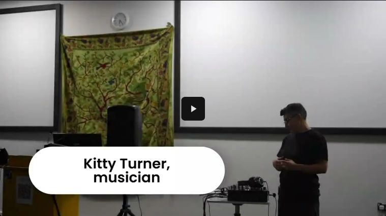 Kitty Turner infront of presenation screens and beside a sound mixer