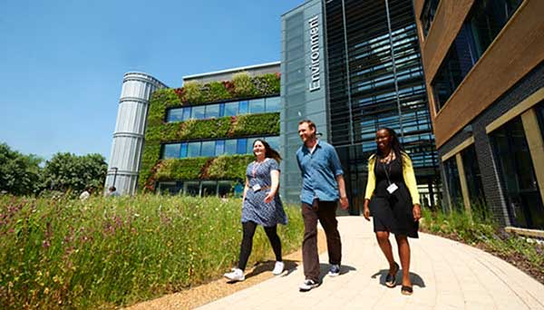 Three students walking past the Environment Building at the University of York, with the living wall in the background.